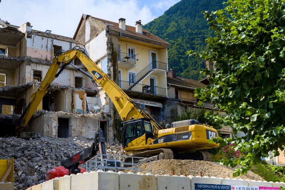 Excavator demolishing building against a scenic mountain backdrop, showcasing urban construction.
